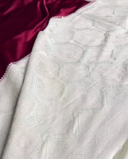 A close-up of a white textured fabric with a raised floral or damask pattern, draped diagonally over a deep magenta satin fabric.